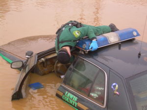 A deputy reaches into a flooded patrol car from its roof.